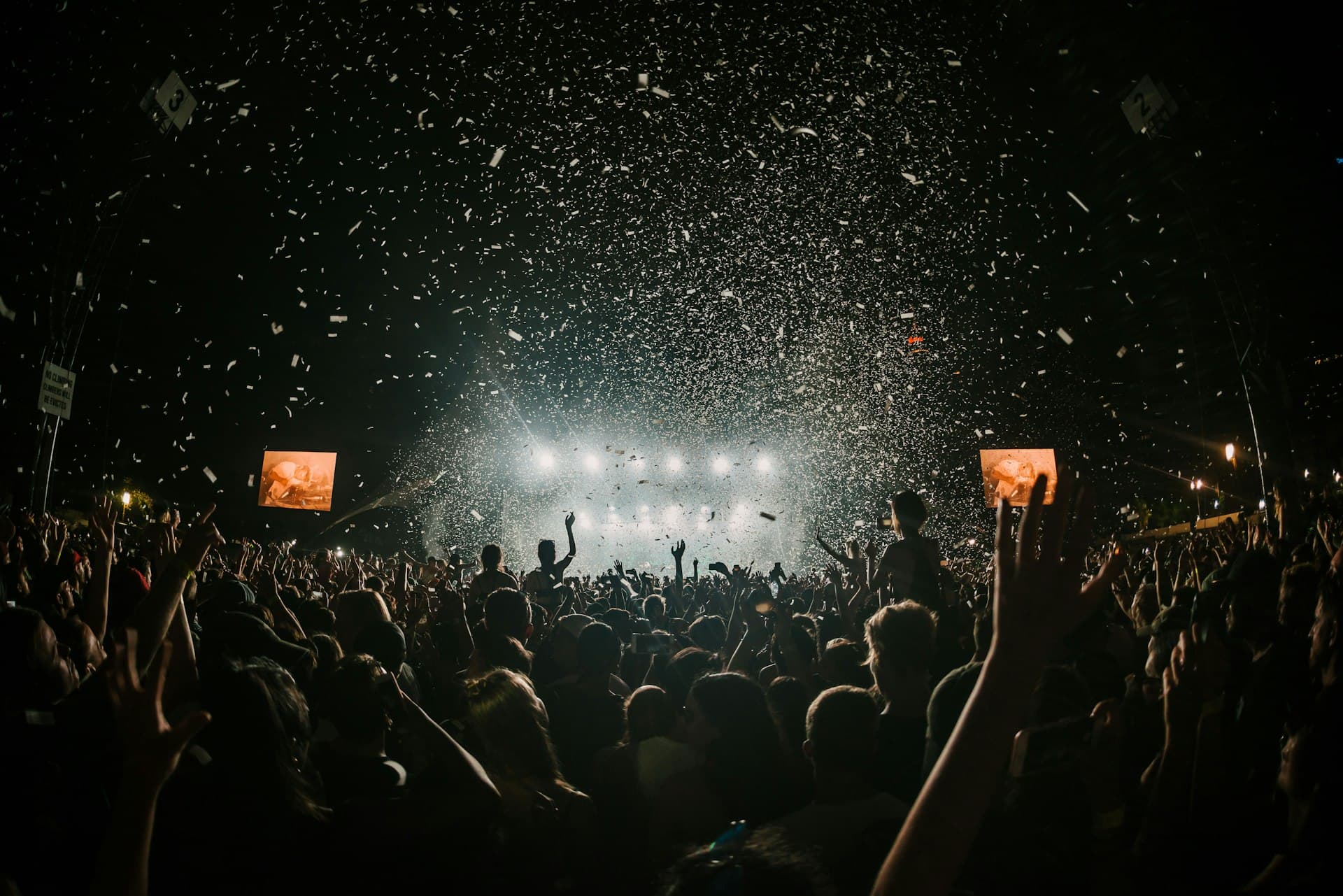 Crowd with hands raised under stage lights and confetti